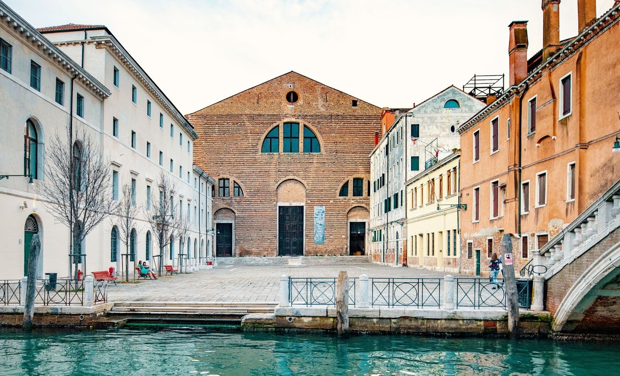 Frontal view of Ocean Space inside the Church of San Lorenzo in Venice, featuring the unfinished brick façade opening onto a small canal-side square, framed by historic buildings in light and warm tones.